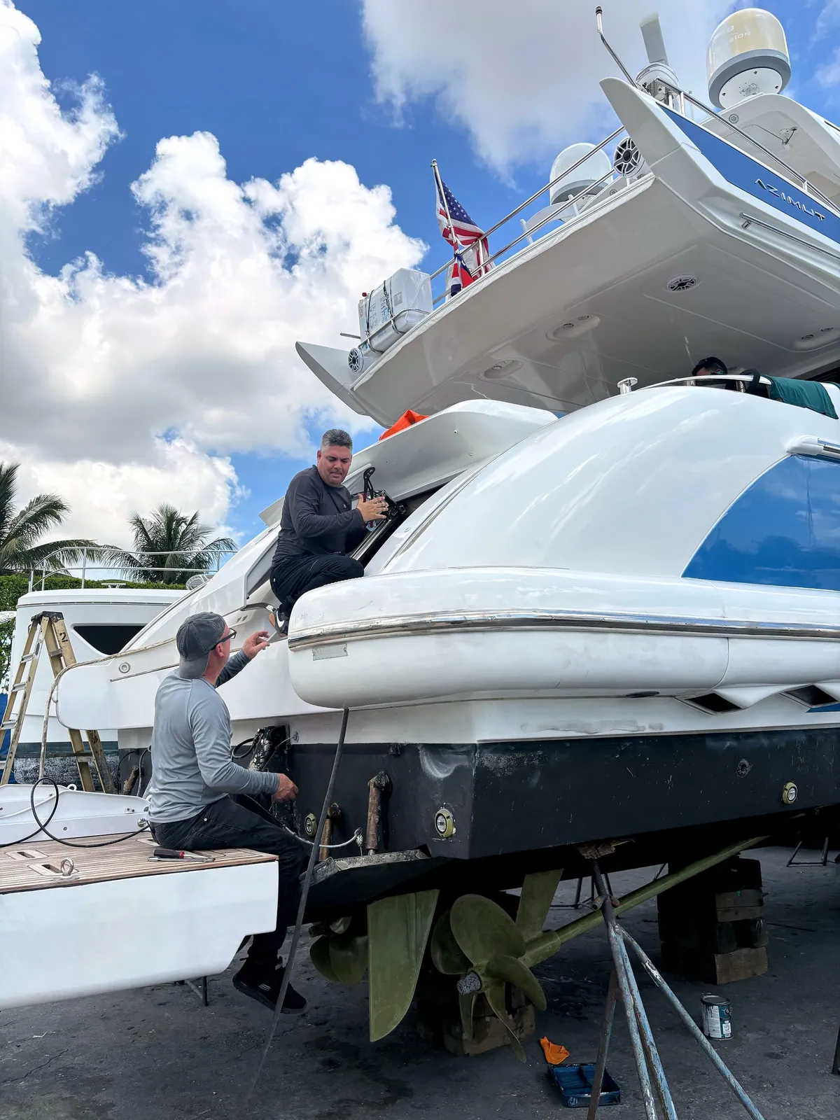 Crew servicing a hauled-out motor yacht's stern and running gear